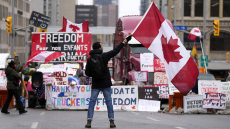 A protester waves a Canadian flag in front of parked vehicles in Ottawa. © AP / Justin Tang