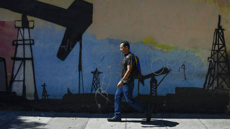 A man walks past a mural featuring oil pumps and wells in Caracas, Venezuela, Friday, Jan. 3, 2020