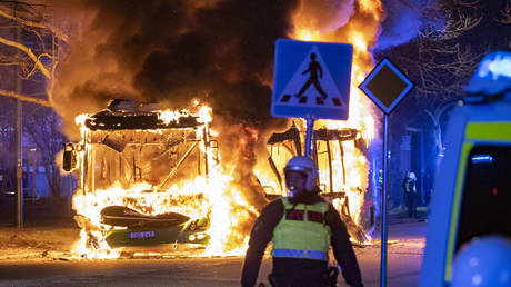 A police officer in riot gear stands in front of a burning bus on April 16, 2022, Malmo, Sweden