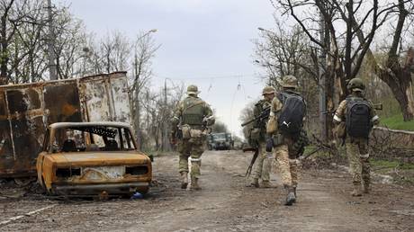 Servicemen of the Donetsk People's Republic militia walk past damaged vehicles during a heavy fighting in an area controlled by separatist forces and the Russian military in Mariupol, Ukraine, April 19, 2022.