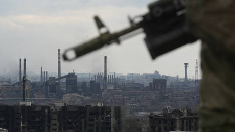 A Russian serviceman holding an assault rifle is seen against the background of the Azovstal steel plant in Mariupol.