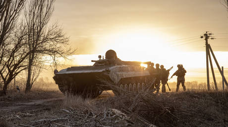Ukrainian servicemen take cover behind a military armored vehicle as they walk towards the battlefield in Lukâyanivka, eastern of Kyiv, Ukraine, March 28th, 2022. © Narciso Contreras / Anadolu Agency via Getty Images
