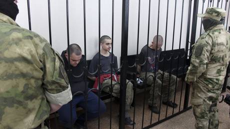 Aiden Aslin (L) and Shaun Pinner (R), and Moroccan Saaudun Brahim (C), sit behind bars in a courtroom in Donetsk, Donetsk People's Republic, June 9, 2022 © AP /