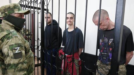 British citizens Aiden Aslin and Shaun Pinner, and citizen of Morocco Saadun Brahim sit inside a defendants' cage as they attend a court hearing in Donetsk, Donetsk People's Republic.