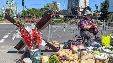 A woman sells vegetables and flowers close to an anti-tank obstacle defense on a street in Kyiv, Ukraine, July 22, 2022
