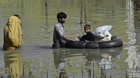 A family wades through a flood-hit area following heavy monsoon rains in Pakistan's Khyber Pakhtunkhwa province. © AFP / Abdul Majeed