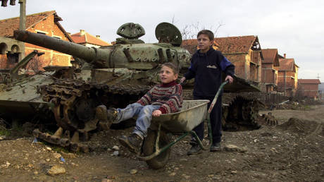 FILE PHOTO. Two Kosovar boys play with a wheelbarrow January 12, 2001 in Klina, Kosovo at one of 112 sites where NATO used armor-piercing shells tipped with depleted uranium during the 1999 bombing of Yugoslavia.