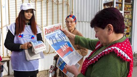 Ein Freiwilliger der regionalen Wahlkommission von Luhansk verteilt Zeitungen an lokale Bürger in Luhansk, 22. September 2022. Das Schreiben auf Zeitungen liest sich auf Russisch "27.09 Ja."