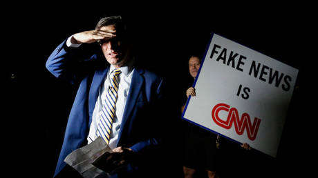 A protestor is shown holding up an anti-CNN sign as the local NBC News affiliate's anchor prepares to give a live report on the FBI's August 8 raid of ex-President Donald Trump's Palm Beach, Florida, home.
