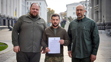 Le président ukrainien Vladimir Zelensky (au centre), le Premier ministre Denis Shmygal (à droite) et le président du Parlement Ruslan Stefanchuk (à gauche) posent avec le document demandant une adhésion accélérée à l'OTAN.