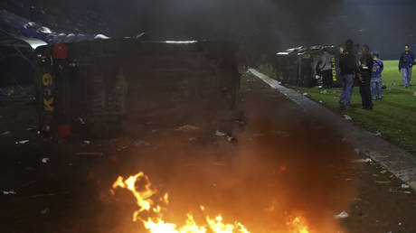 Plain-clothed officers stand near the wreckage of police vehicles damaged during a clash between supporters of two Indonesian soccer teams at Kanjuruhan Stadium in Malang, East Java, Indonesia, October 1, 2022