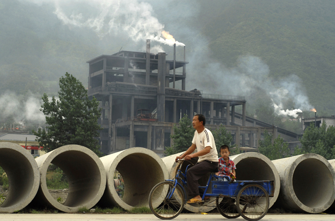 A man rides a tricycle with his son past a cement plant in Baokang. (Reuters)