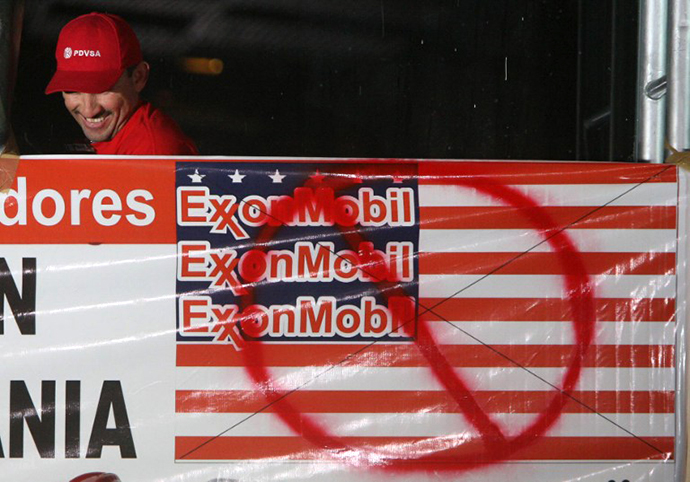 A Petroles de Venezuela (PDVSA) worker smiles next to a banner against ExxonMobil during a meeting to celebrate the court decision against US giant ExxonMobil, at the Simon Bolivar hall in PDVSA's La Campina headquarters in Caracas on March 24, 2008. (AFP Photo / Pedro Rey)