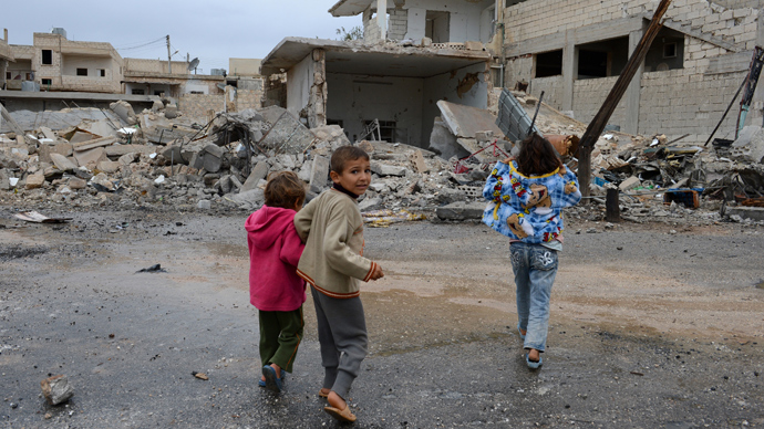 Syrian children walk past buildings destroyed in an air strike by regime forces on the northern Syrian town of Taftanaz, in the Idlib province (AFP Photo / Philippe Desmazes)