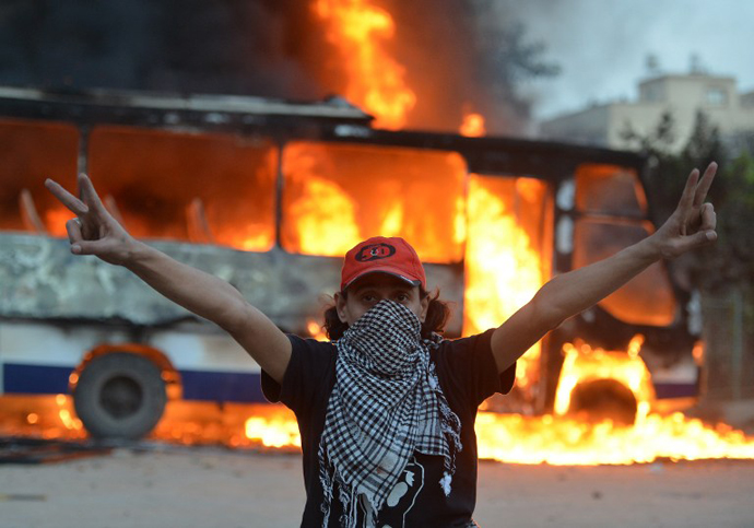 An Egyptian protester flashes the sign of victory in front of a bus belonging to the Egyptian Muslim Brotherhood on fire during clashes near the movements' headquarters in Cairo on March 22, 2013. (AFP Photo / Haled Desouki)