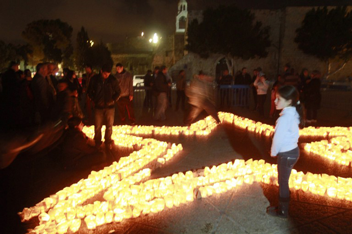 A child looks on as members of Palestine Wildlife Society outline the star of Bethlehem with candles at the Manager Square in front of the Church of the Nativity in the West Bank town of Bethlehem on March 23, 2013, to mark the Earth Hour for the first time in Palestine. (AFP Photo / Musa al-Shaer)