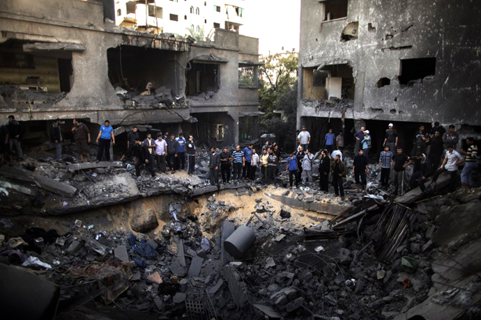 Palestinian men gather around a crater caused by an Israeli air strike on the al-Dallu family's home in Gaza City on November 18, 2012. (AFP Photo / Marco Longari)