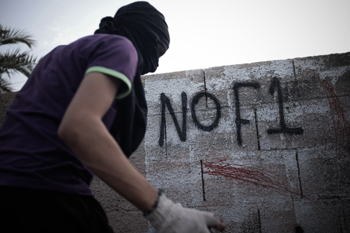 A Bahraini masked protestor writes graffiti against the upcoming Bahrain Formula One Grand Prix on the sidelines of an anti-regime rally in support of political activists held in jail in the village of Jid Ali, north-east of Isa Town, on April 17, 2013 (AFP Photo / Mohammed Al-Shaikh) 