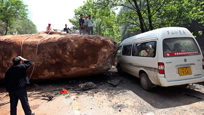 People stand near a van on a road blocked by a large rock after a strong 6.6 magnitude earthquake, at Longmen village, Lushan county, Ya'an, Sichuan province April 20, 2013.(Reuters / Stringer)