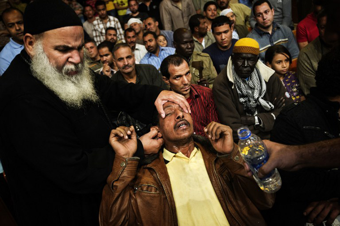 An Egyptian man reacts after being sprayed with holy water by Coptic priest Abraam Fahmi (left) during a function on April 25, 2013 at the St Samaans (Simon) Church. (AFP Photo / Gianluigi Guercia)