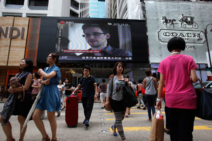 People cross a street in front of a monitor showing file footage of Edward Snowden, a former contractor for the U.S. National Security Agency (NSA), with a news tag (L) saying he has left Hong Kong, outside a shopping mall in Hong Kong (Reuters / Bobby Yip)