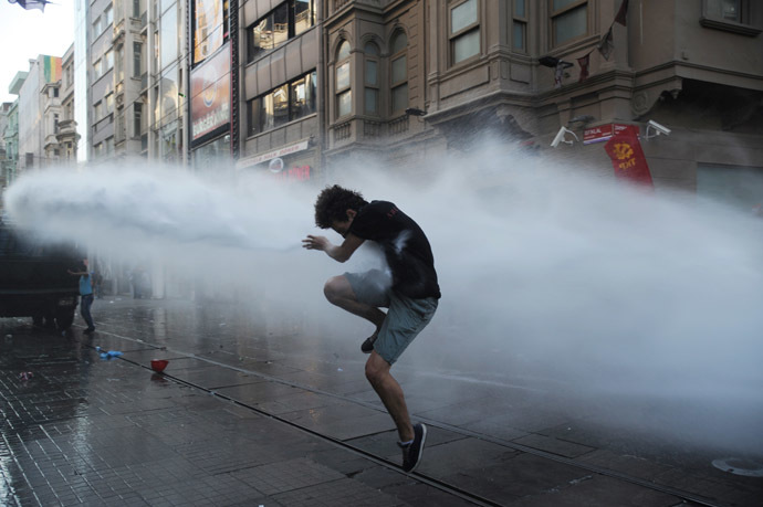 A protesters takes cover from a water cannon jet during clashes with police on Istiklal Avenue in Istanbul on July 6, 2013. (AFP Photo/Bulent Kilic)