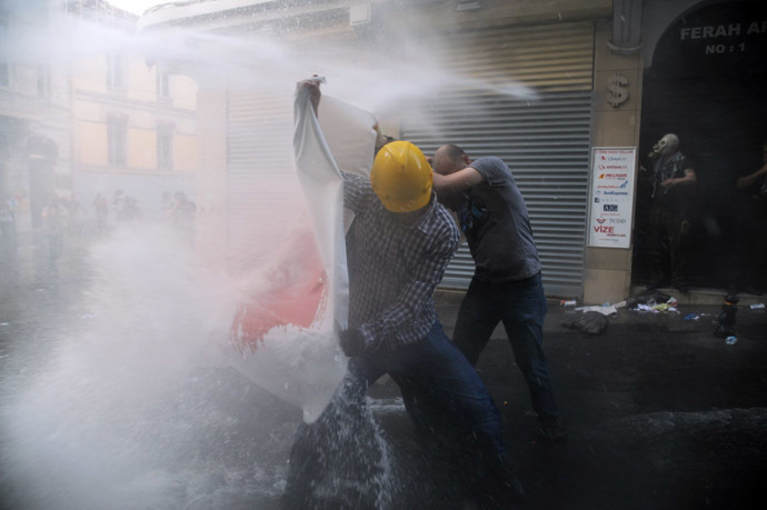 Protesters take cover from a water cannon during clashes with police on Istiklal Avenue in Istanbul on July 6, 2013. (AFP Photo/Bulent Kilic)