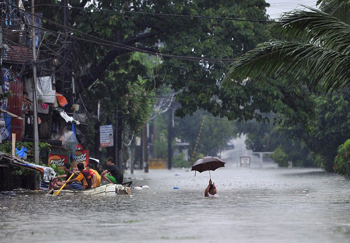 A resident (R) wades through chest-deep floodwaters along a street while his neighbours (L) paddle an improvised life raft in Manila on September 23, 2013, after torrential rains pounded Luzon island worsened by Typhoon Usagi. (AFP Photo / Ted Aljibe)