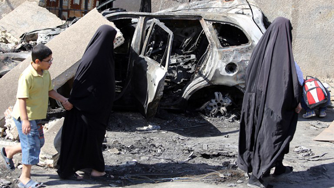 Iraqi women wlak past a burnt-out vehicle on October 7, 2013 following a bombing attack in Baghdad's eastern al-Jadidah district the night before. (AFP Photo / Ahmad al-Rubaye)
