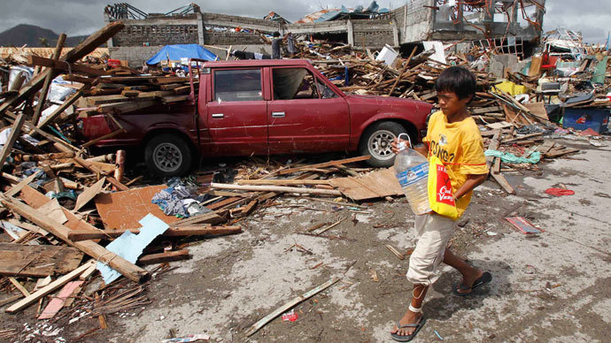 A boy carrying a plastic bottle of water walks past a car which slammed into damaged houses after super Typhoon Haiyan battered Tacloban city, central Philippines November 10, 2013.(Reuters / Romeo Ranoco)