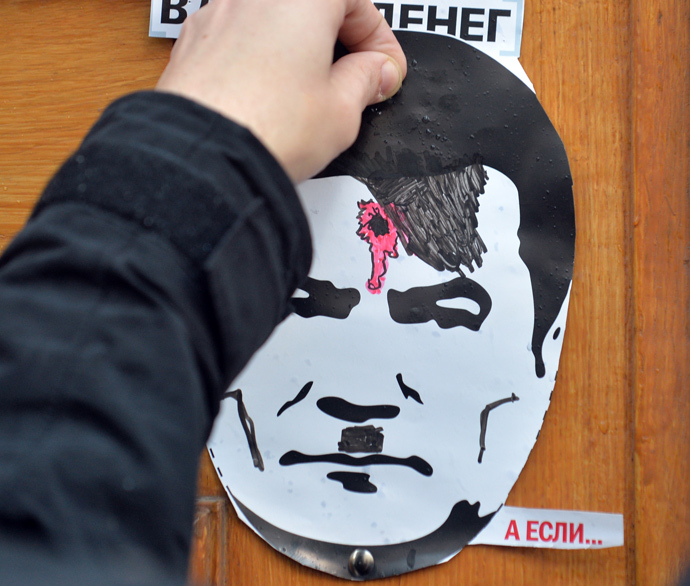 A man attaches a poster with a portrait of the President Viktor Yanukovych depicted as Adolh Hitler with a bullet hole in his head as the protesters block the Ukrainian Cabinet of the Ministers building in Kiev on December 2, 2013. (AFP Photo / Sergei Supinsky)