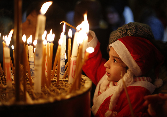 A child wearing a Santa Claus costume lights a candle inside the Church of the Nativity in the West Bank town of Bethlehem during the Eastern Orthodox Christmas January 6, 2014. (Reuters / Mohamad Torokman)
