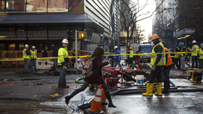 A woman jumps over water being pumped out of a hole in the street, caused by a water main break on January 15, 2014 in New York City. (AFP Photo / Andrew Burton)