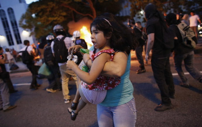 A woman carries her daughter away from their car, after it caught fire driving through a flaming barrier during a protest against the 2014 World Cup in Sao Paulo January 25, 2014. (Reuters/Nacho Doce)