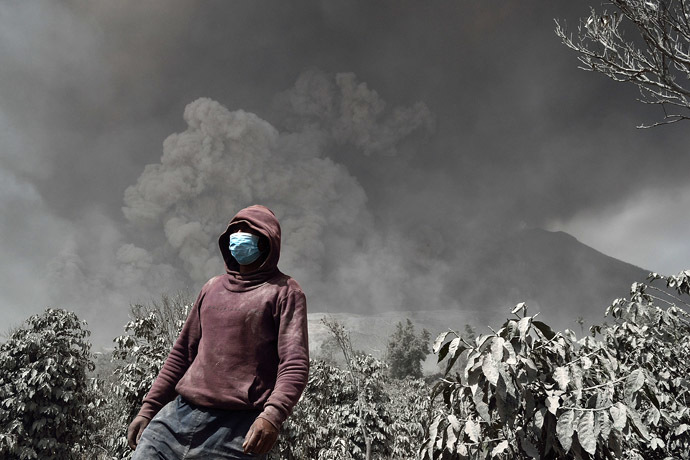 An Indonesian man wearing a mask stands against Sinabung volcano while it spews thick smoke and hot ash in Karo on January 16, 2014. (AFP Photo)