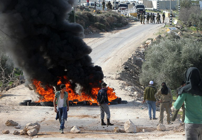 Palestinian protesters stand behind burning tyres in front of Israeli security forces during clashes following a protest against the demolition of a furniture factory which the Israeli authorities said was built without a permit on January 20, 2014 in the village of Deir Samet near the town of Hebron, in the occupied West Bank. (AFP Photo / Hazem Bader)