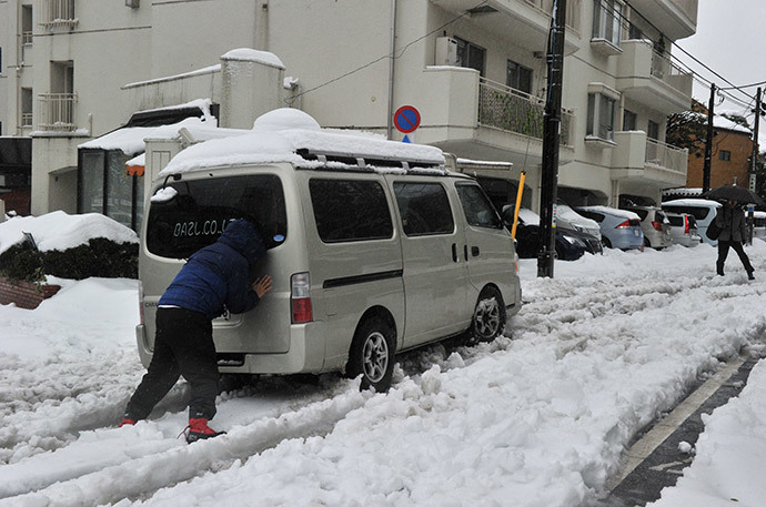 A man pushes a vehicle after it lost traction and skidded on a snow covered road in Tokyo on February 15, 2014 as trafic is disrupted after a heavy snowfall. (AFP Photo / Yoshikazu Tsuno)