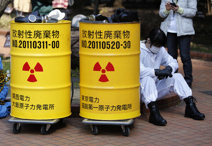An anti-nuclear protester wearing protective suit sits next to mock drums labelled as radioactive waste from Kansai Electric Power Co's Ohi nuclear power plant (L) and Tokyo Electric Power Co's (TEPCO) Fukushima nuclear power plant, before a march in Tokyo March 9, 2014.(Reuters / Yuya Shino)