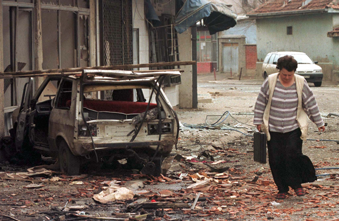 A woman passes a destroyed car March 28,1999 after a NATO missile hit downtown of Kosovo's capital of Pristina in Saturday night's NATO attack (Reuters)