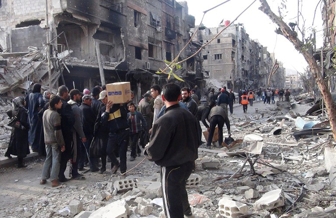 Residents of Syria's besieged Yarmuk Palestinian refugee camp, south of Damascus, stand amidst debris as they wait to receive food parcels on March 24, 2014. (AFP Photo / Rami Al-Sayed)