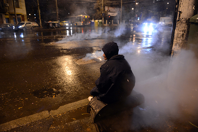 A homeless person warms-up at an air pit of a heating system in Bucharest. (AFP Photo / Daniel Mihailescu)
