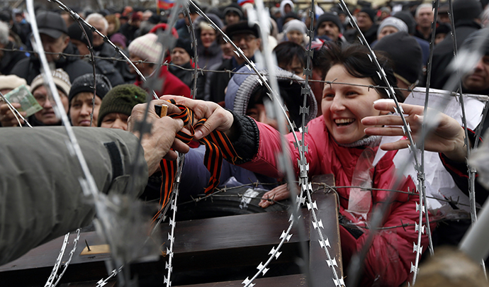 A pro-Russian activist reaches through razor wire to receive a ribbon of St. George, a well-known Russian symbol of military valor which has become a symbol of pro-Russian protesters, at a barricade outside the regional state administration building in Donetsk, eastern Ukraine, on April 12, 2014. (AFP Photo / Max Vetrov)