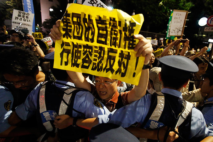 A protester holding a placard shouts slogans at a rally against Japan's Prime Minister Shinzo Abe's push to expand Japan's military role as police officers refrain him in front of Abe's official residence in Tokyo June 30, 2014 (Reuters / Yuya Shino)