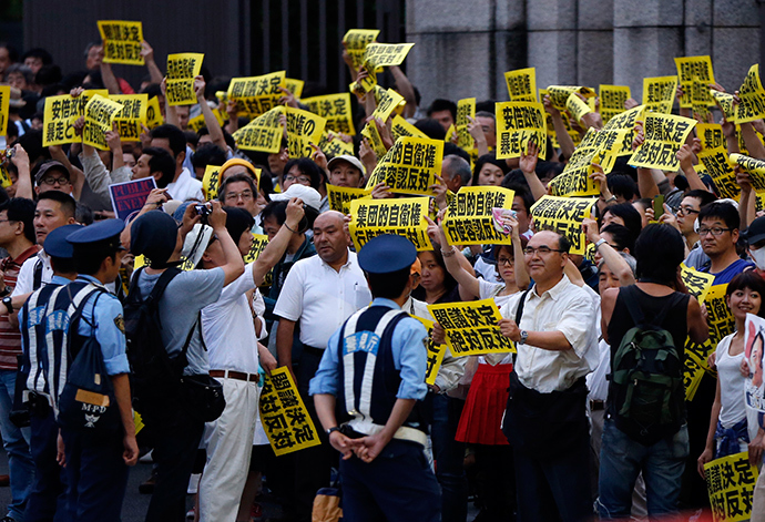 Protesters holding placards shouts slogans as they gather at a rally against Japan's Prime Minister Shinzo Abe's push to expand Japan's military role while police officers stand guard in front of Abe's official residence in Tokyo June 30, 2014 (Reuters / Issei Kato)