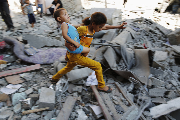 A Palestinian girl carries a child across rubble from a building that police said was destroyed by an Israeli air strike, in the Burij refugee camp in the central Gaza Strip (Reuters / Finbarr O'Reilly)