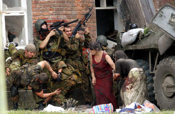 A Russian special police soldier (L) carries an injured colleague as two soldiers and two women take cover behind the APC during the rescue operation of Beslan's school, northern Ossetia, 03 September 2004. (AFP Photo/Yuri Tutov)