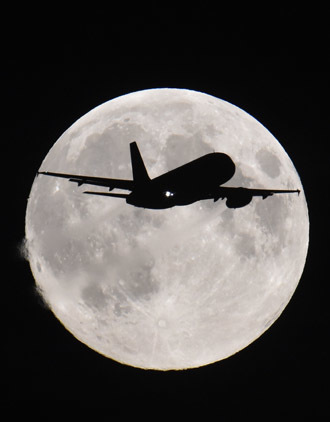A passenger aircraft descends towards Heathrow Airport with a full moon seen behind, in west London, September 8, 2014. (Reuters/Toby Melville)