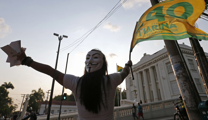 A supporter of Brazilian Socialist Party (PSB) presidential candidate Marina Silva, with a Guy Fawkes mask strapped to the back of her head, waves a campaign flag in front of the Rio Branco Palace in Rio Branco, Acre state October 3, 2014. (Reuters/Sergio Moraes)