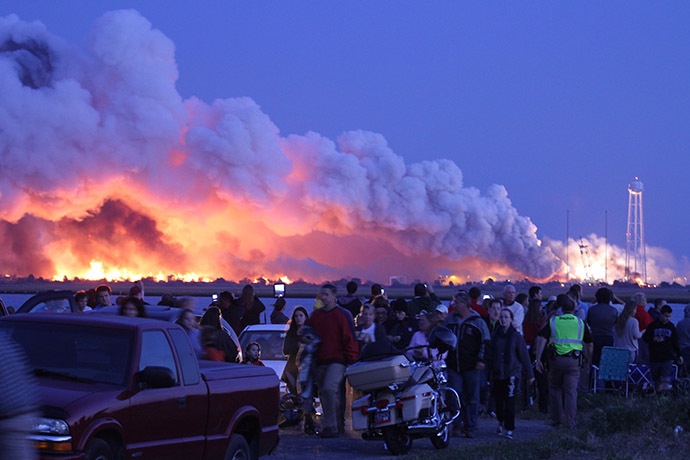 People who came to watch the launch walk away after an unmanned rocket owned by Orbital Sciences Corporation exploded (background) October 28, 2014. (AFP Photo/Steve Alexander)