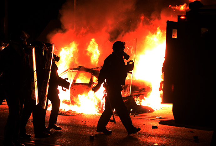 Police chase protesters passing by one of their burning cars during clashes following the grand jury decision in the death of 18-year-old Michael Brown in Ferguson, Missouri, on November 24, 2014 (Reuters / Jewel Samad)